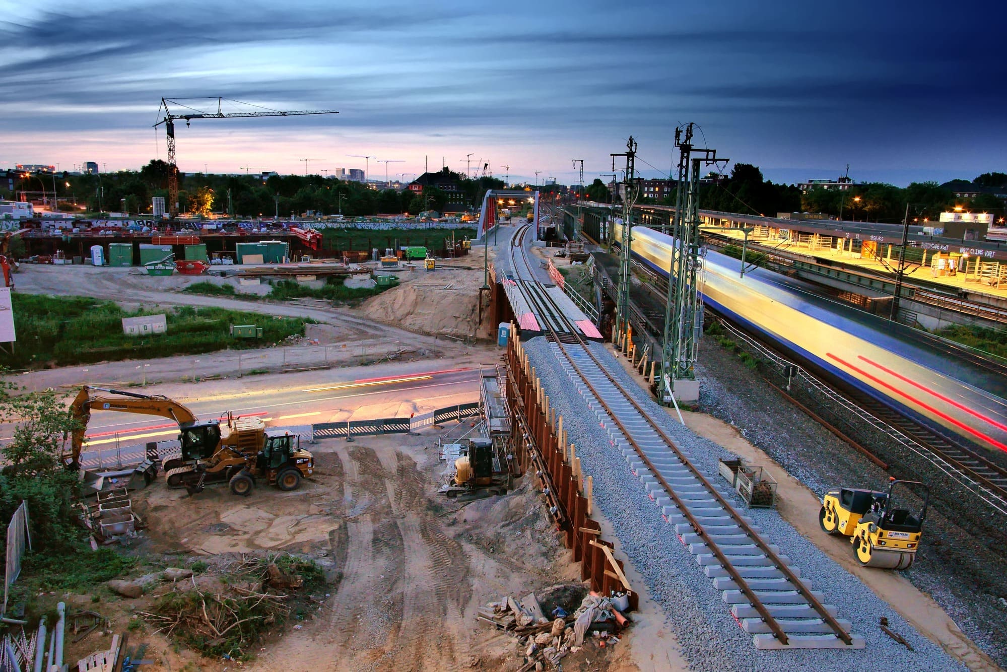 Abendliche Baustelle an Eisenbahnstrecke, daneben Gleise und ein Bahnsteig.