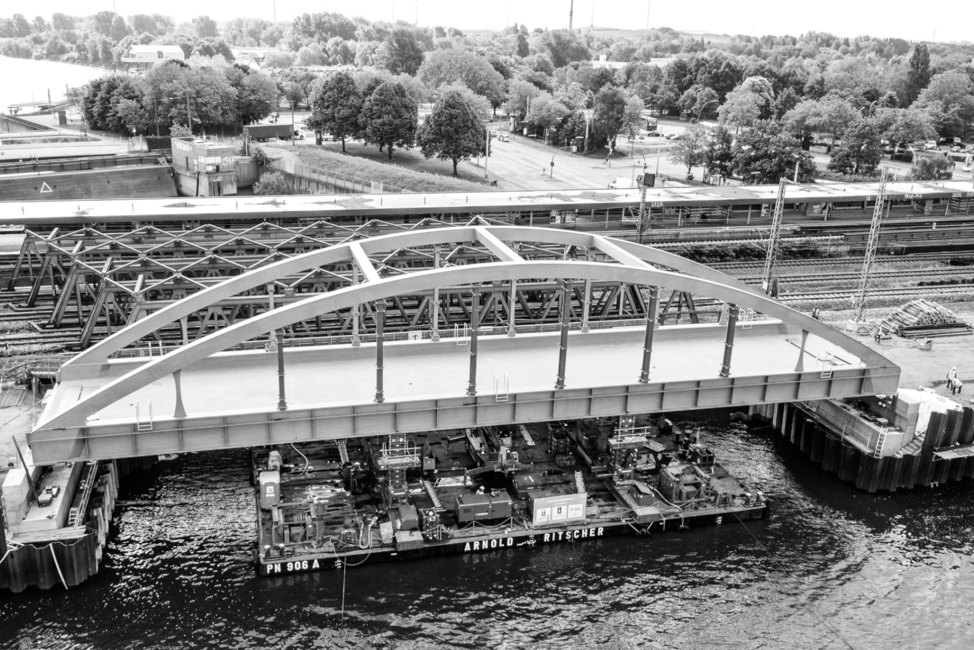 Schwarz-weiß-Aufnahme einer Bogenbrücke, darunter eine schwimmende Plattform mit Hubeinrichtung