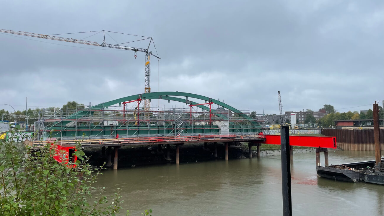 Die blaue Stabbogenbrücke der Harburger Chaussee mit Baugerüst und Kran.